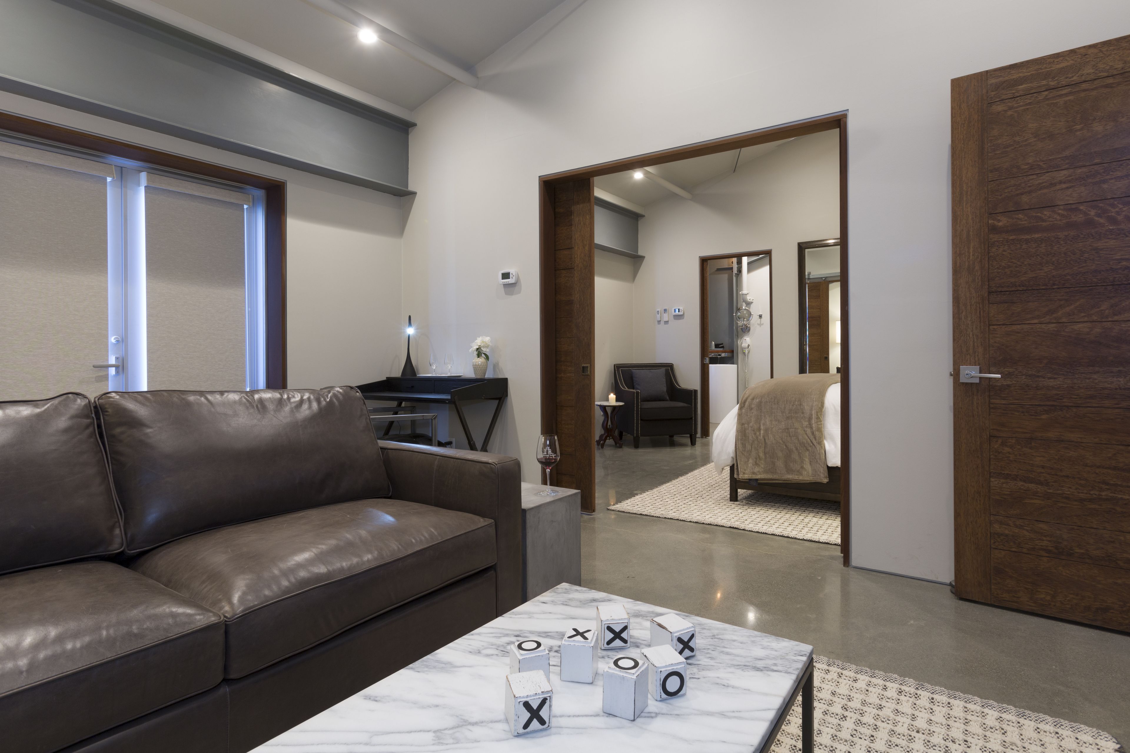 A modern living room with a leather sofa, a marble coffee table with alphabet blocks, and a view into a bedroom through an open door.