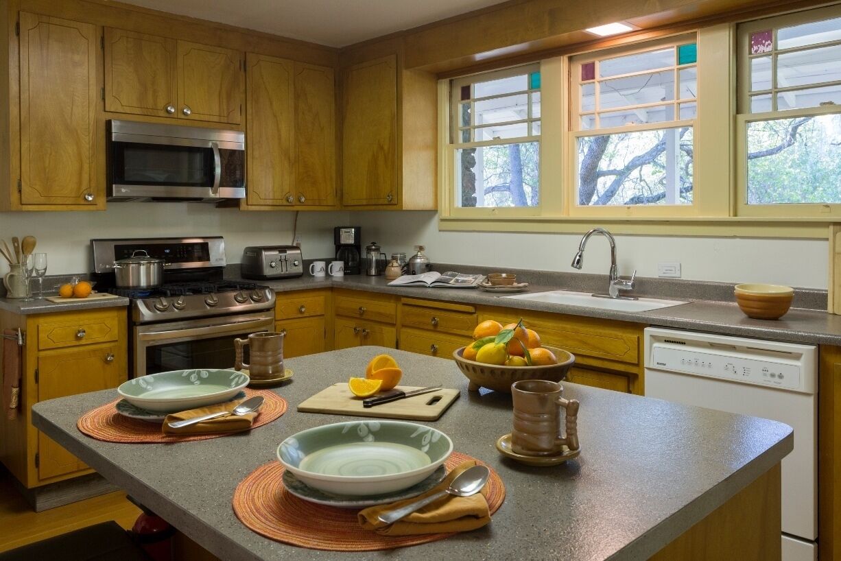 Une cuisine avec des meubles en bois, un four à micro-ondes, une cuisinière et une fenêtre donnant sur les arbres.