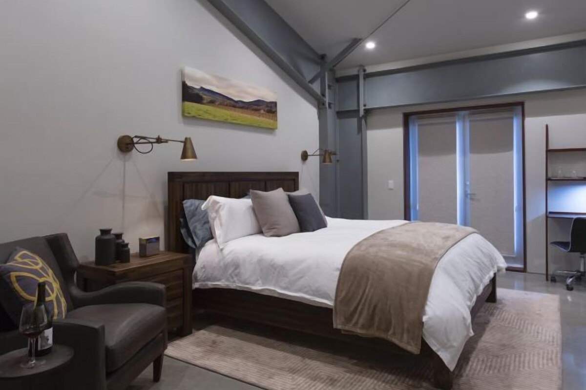 Un dormitorio moderno con una cama grande, una mesita de noche, una silla y un cuadro en la pared.