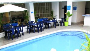 Une piscine avec un espace de jacuzzi carrelé, des sièges extérieurs et des plantes en pot.