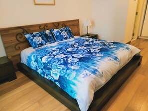 A bedroom with a wooden headboard, a bed with a blue floral bedspread, a bedside table with a lamp, and a nightstand.