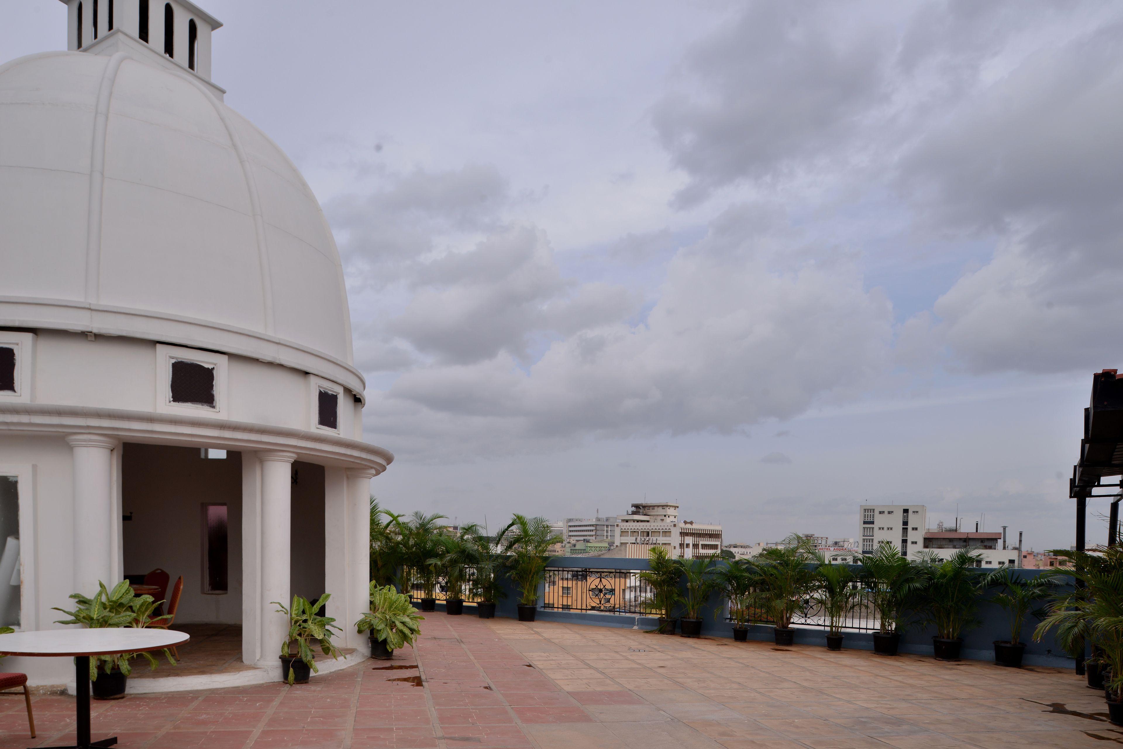 A rooftop terrace with a white dome structure, potted plants, and a view of the cityscape in the background.