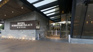 La entrada del Hotel Eurostars Palace, con un diseño moderno, presenta un acceso de vidrio y un cartel con el nombre del hotel y su categoría.