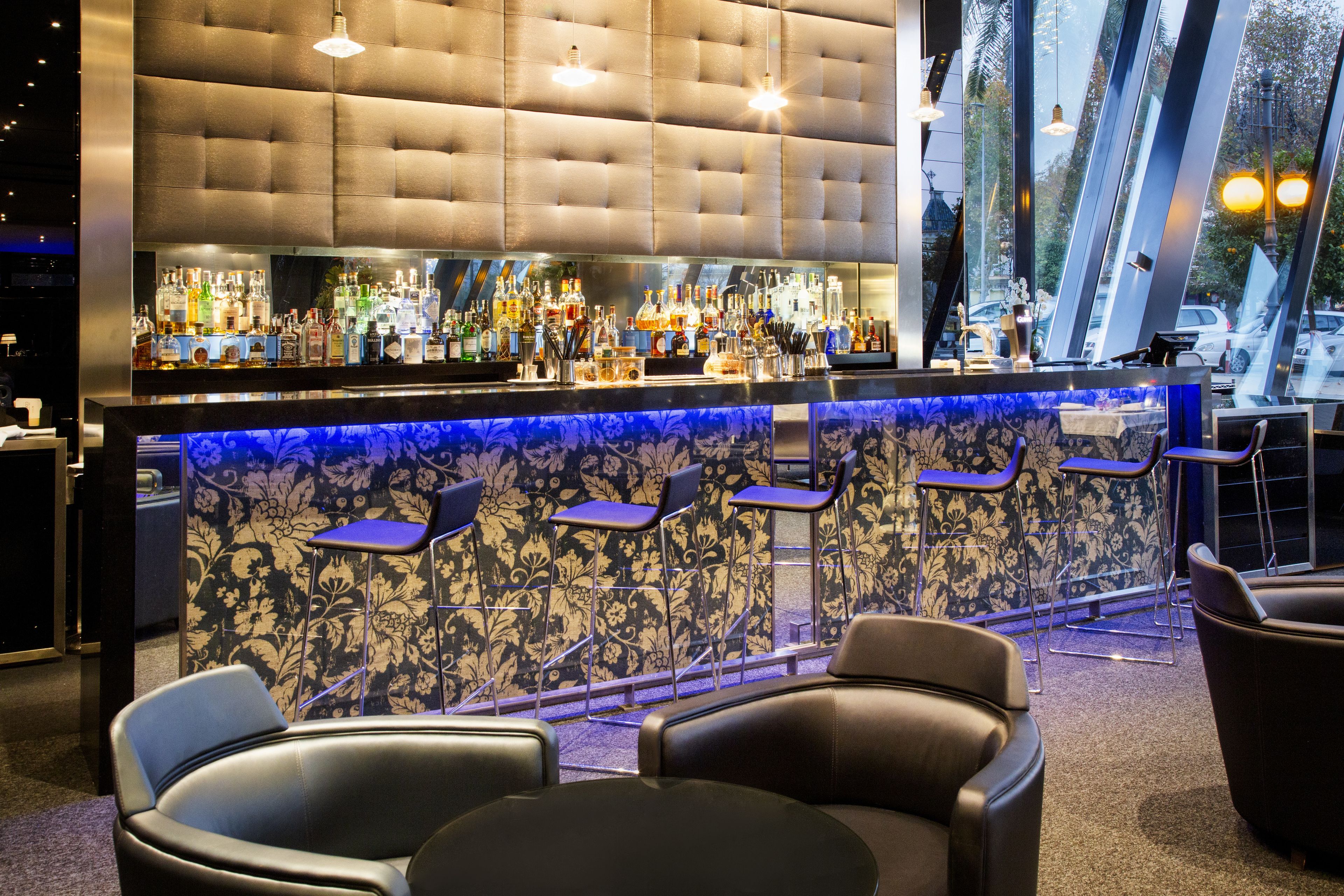 A bar area with a tufted backrest, a bar counter with a blue floral pattern, and several bar stools.