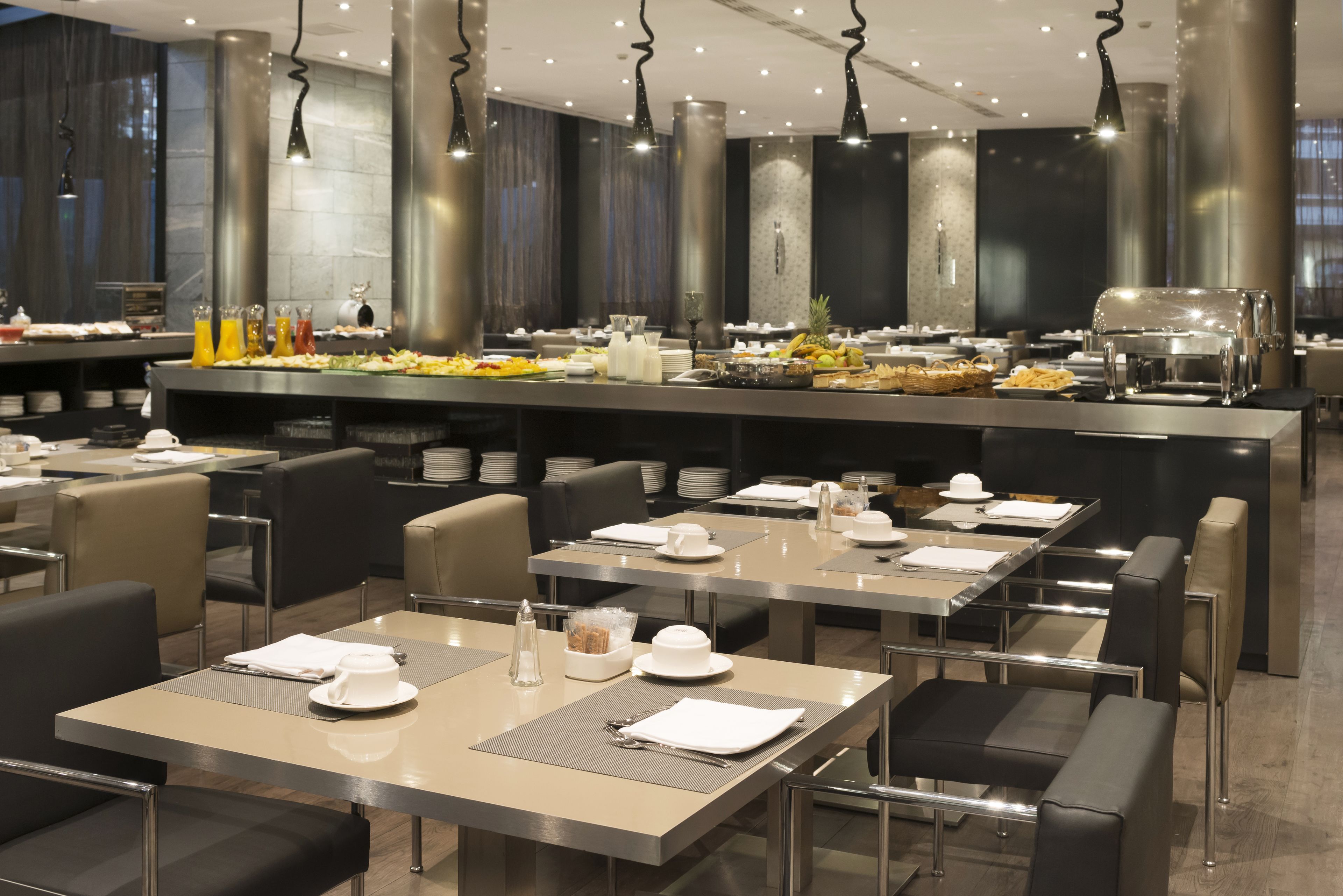 A modern dining area with tables set for breakfast, a buffet line, and a coffee station.