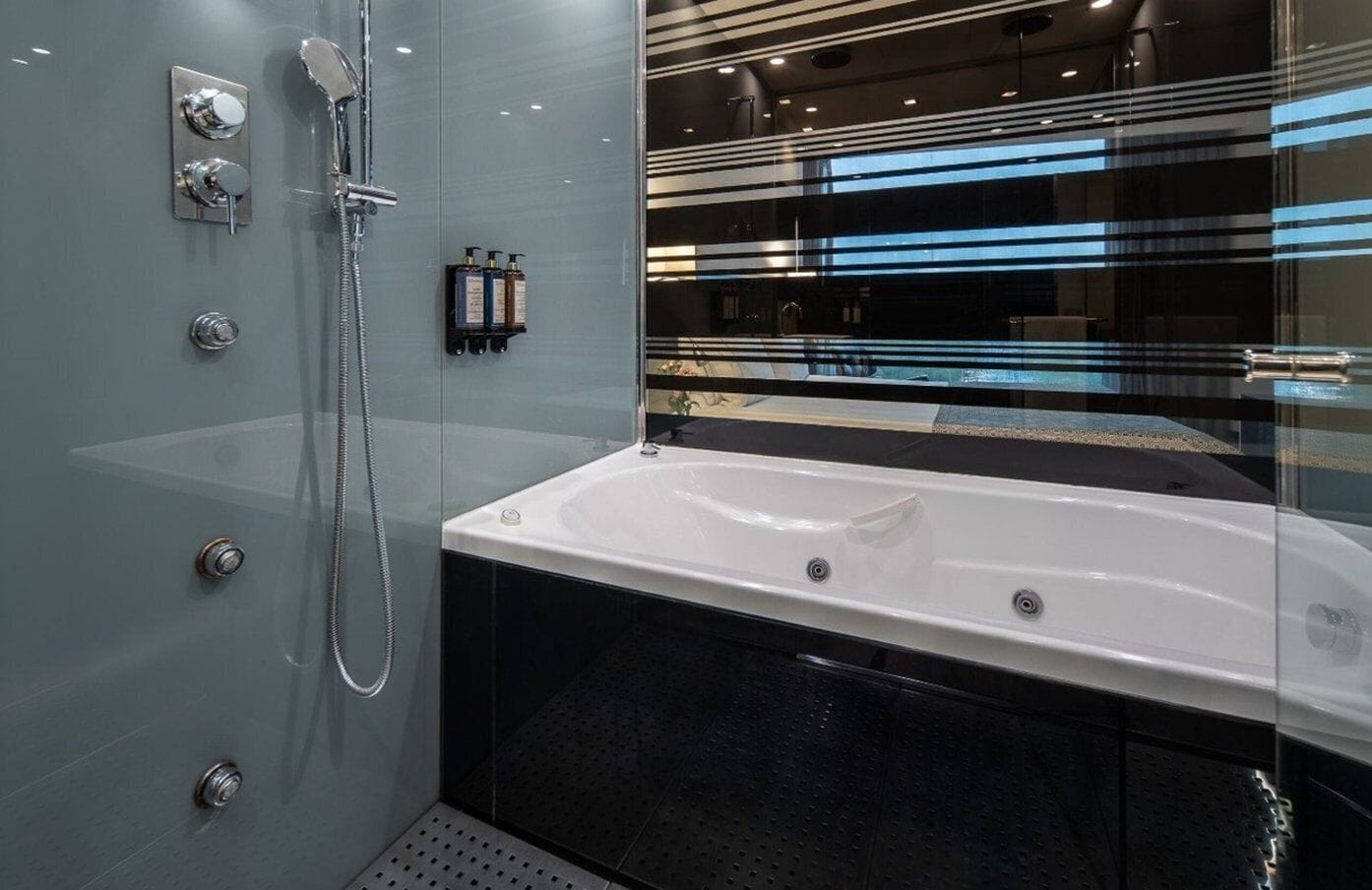 Un baño moderno con ducha envuelta en cristal, una bañera blanca y suelo de baldosas negras.