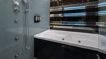 Un baño moderno con ducha envuelta en cristal, una bañera blanca y suelo de baldosas negras.