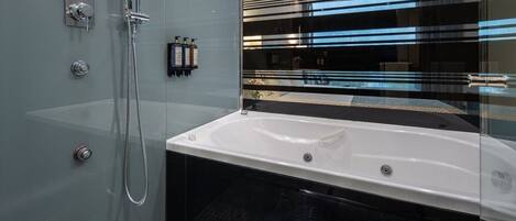 Un baño moderno con ducha envuelta en cristal, una bañera blanca y suelo de baldosas negras.