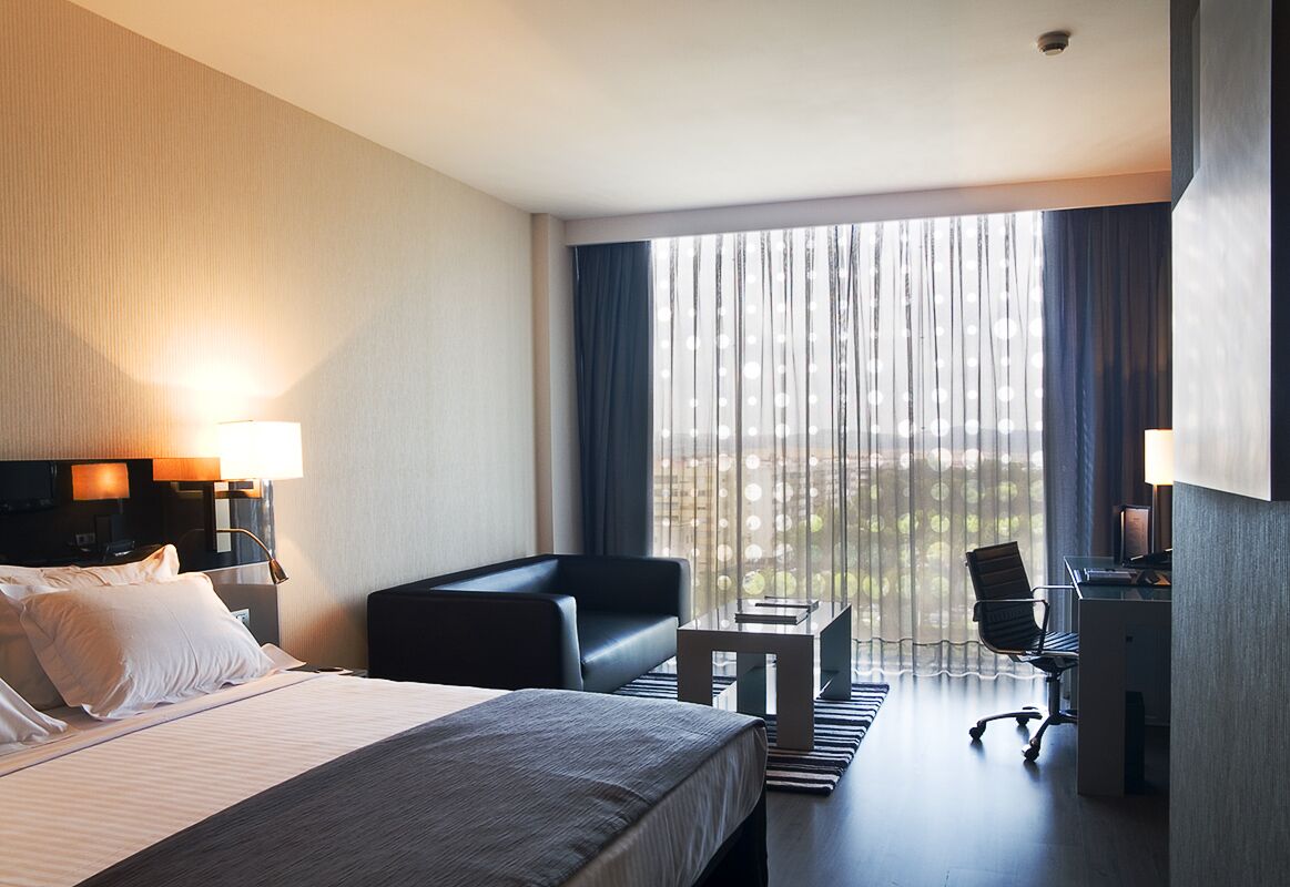 Une chambre d’hôtel avec un grand lit, un bureau, une chaise et une vue par la fenêtre.