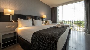 Una habitación de hotel moderna con una cama grande, lámparas de noche, una mesita de noche y vistas de la ciudad a través de amplios ventanales.