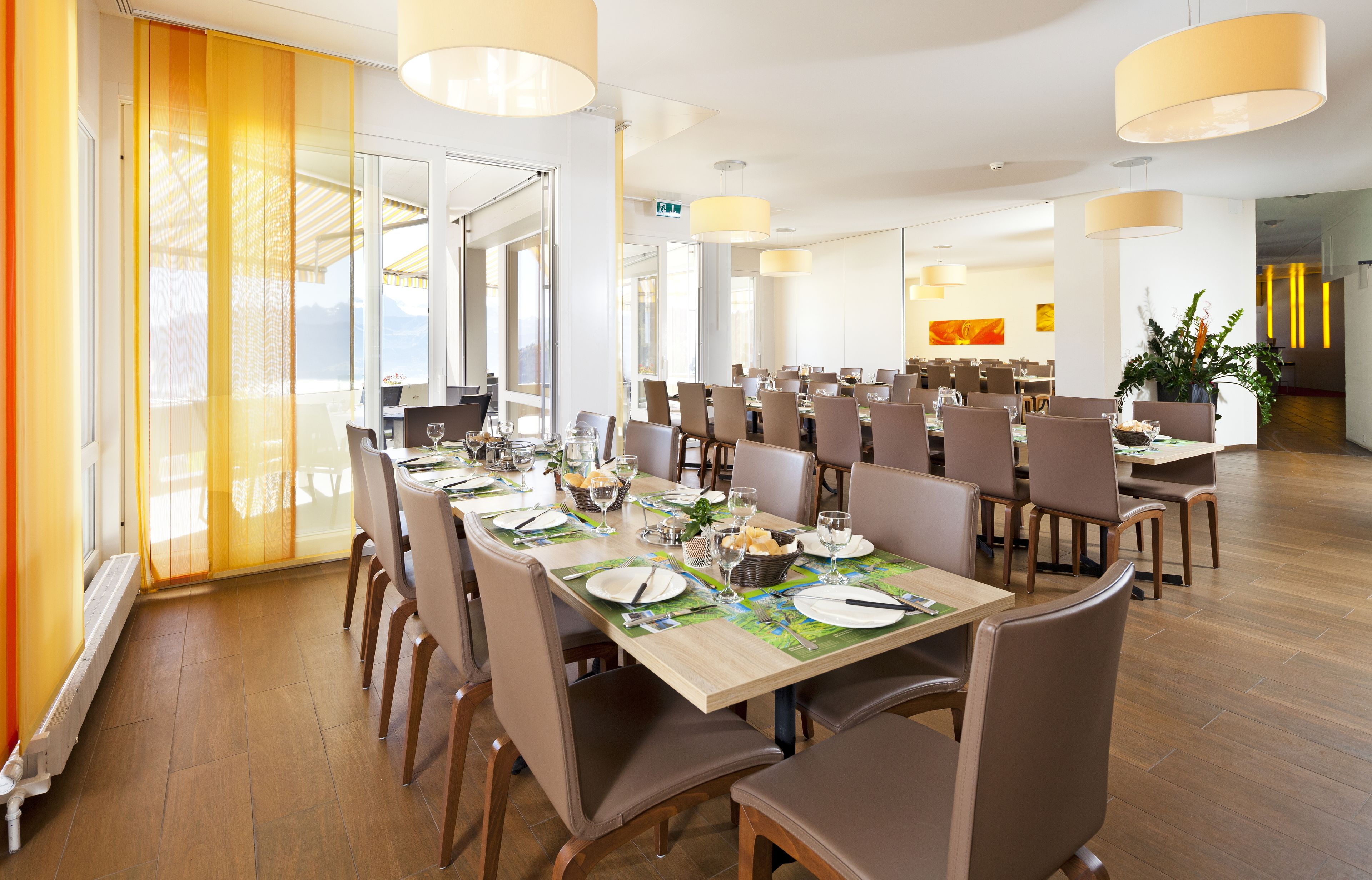 A spacious dining area with multiple tables set for meals, large windows, and a modern interior design.