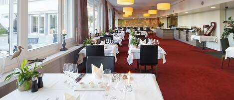 A restaurant with tables set for dining, large windows, and a red carpet.