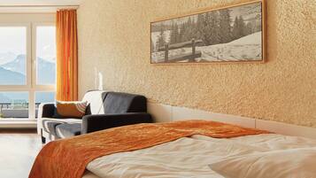 Habitación de hotel con cama, una silla, ventana con cortinas e imagen enmarcada en la pared.