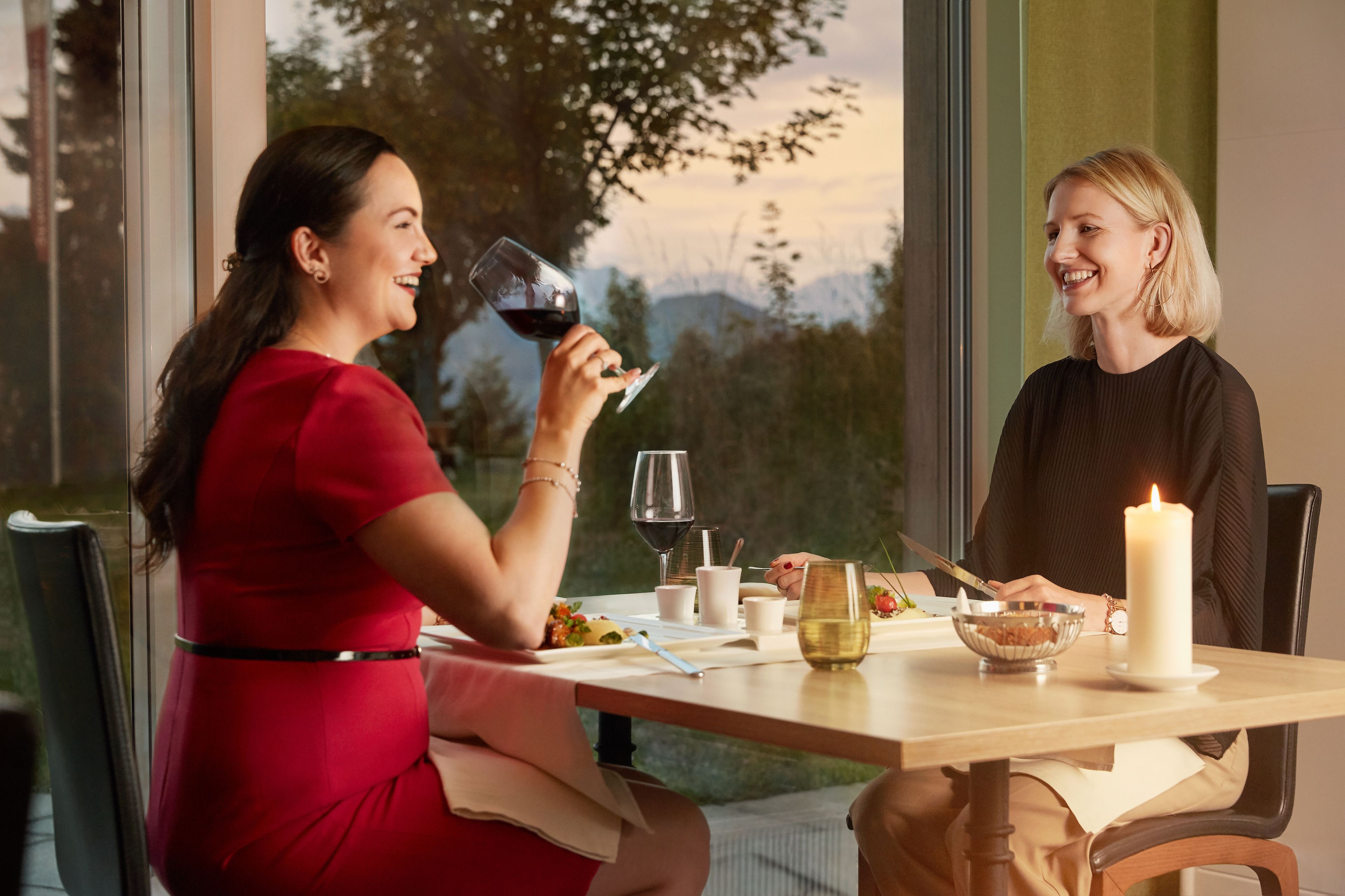 Two people dining at a table with a candle, wine glasses, and a bowl of nuts.