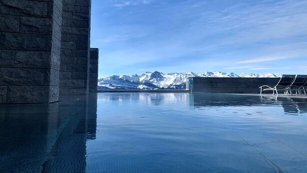 En pool med utsikt över bergen, omgiven av stenmurar och med bekväma solstolar.