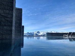 Piscina con vistas a la montaña, paredes de piedra y sillones de descanso.