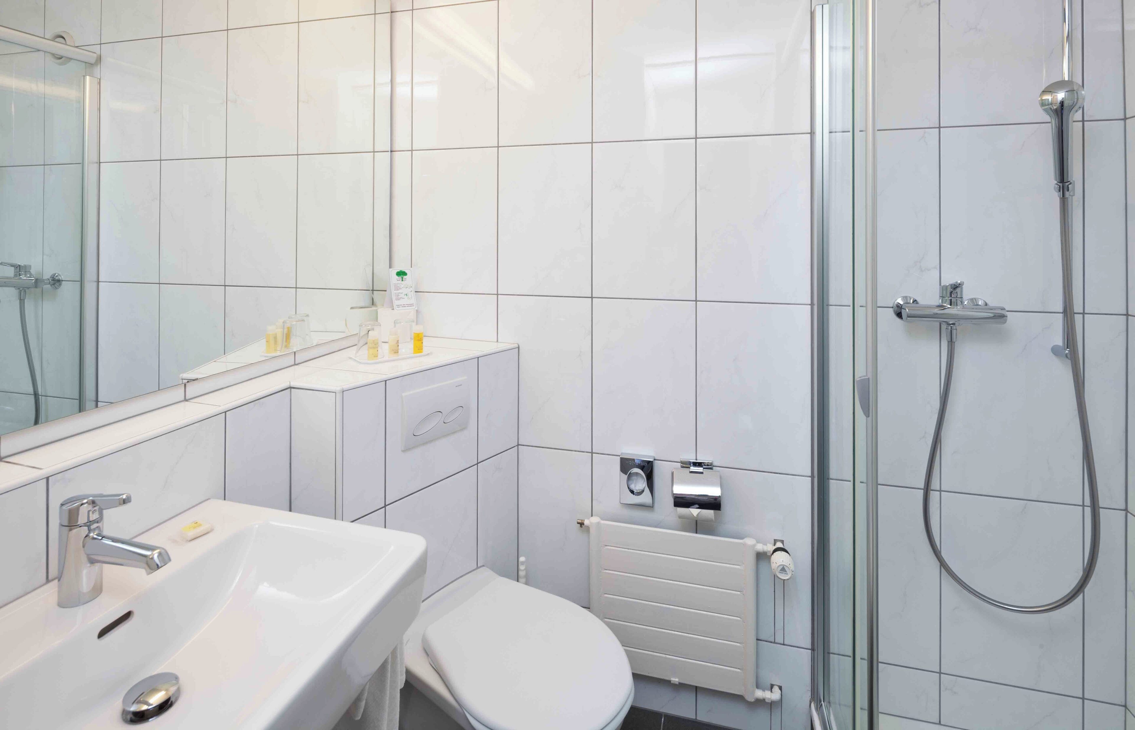 Un baño moderno con ducha, lavabo, inodoro y espejo.