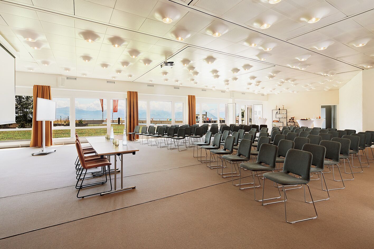 Un salón de conferencias con filas de sillas, un atril y un ventanal con vistas.