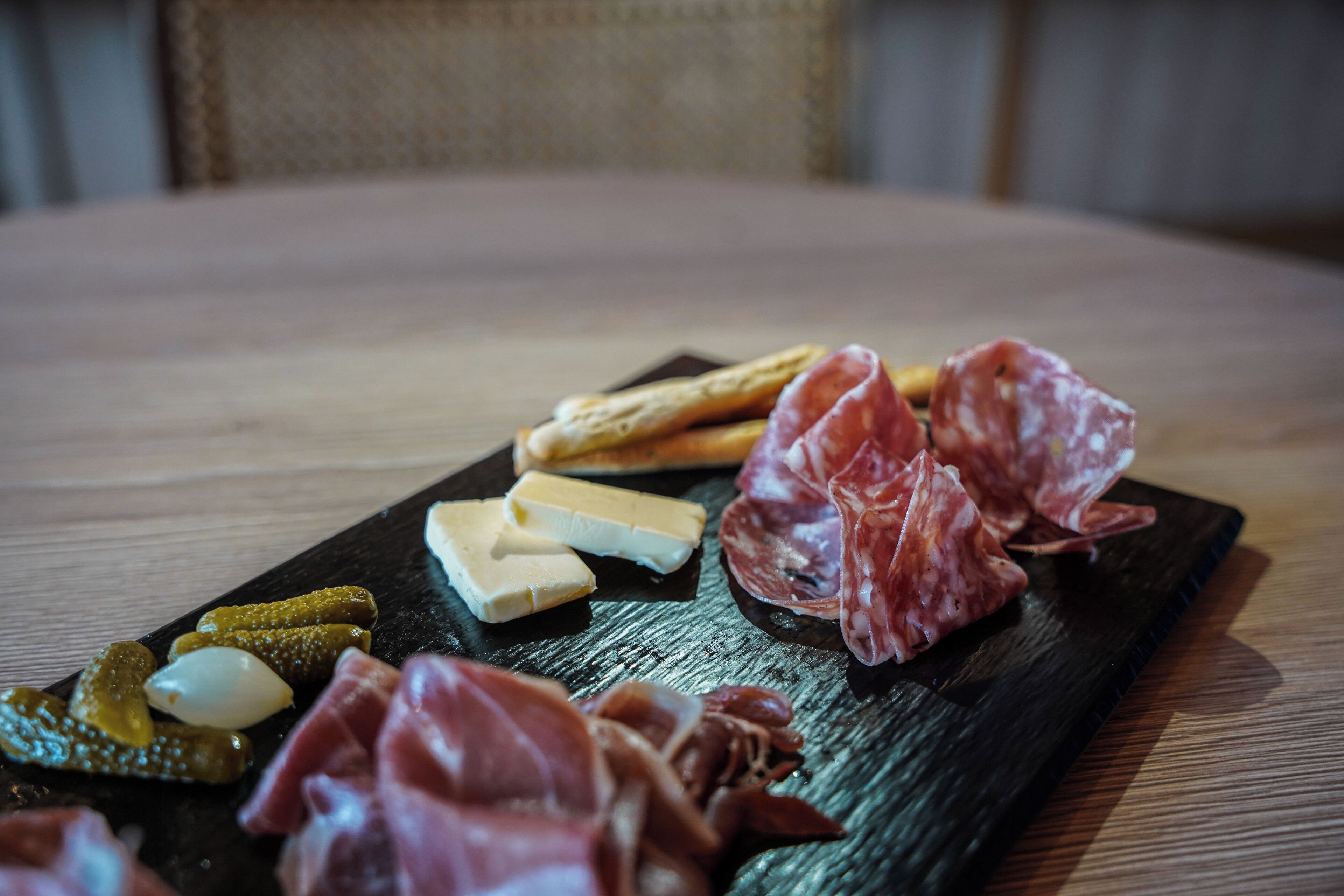 Une planche de charcuterie comprenant différentes sortes de viandes, de fromages et de cornichons, présentée sur une ardoise sombre.