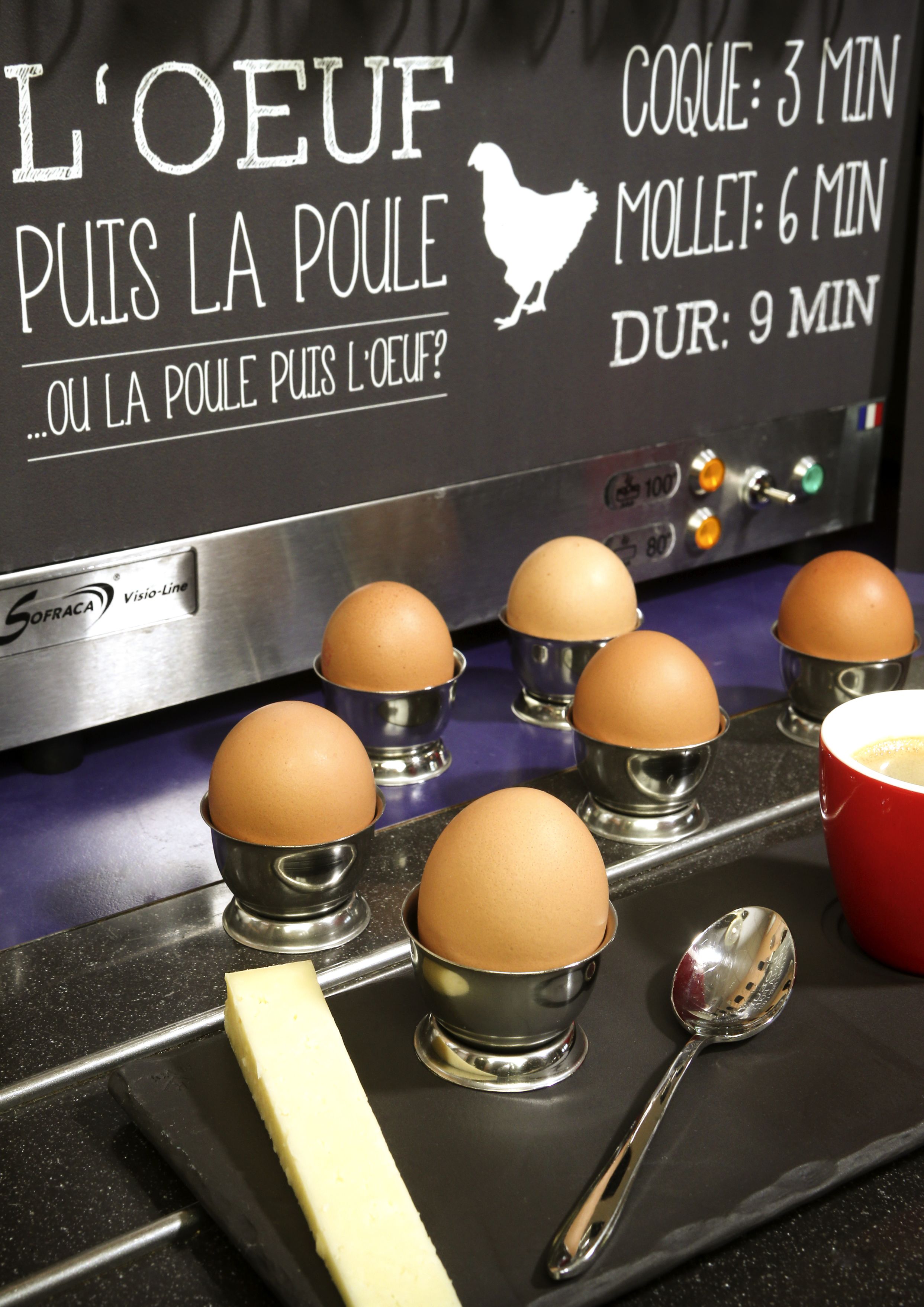 A kitchen counter with eggs in metal cups, a cheese block, and a red cup.