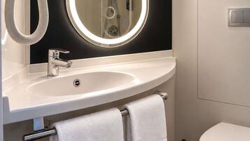 A modern bathroom with a white sink, a mirror with a light halo, a handheld showerhead, and a toilet.