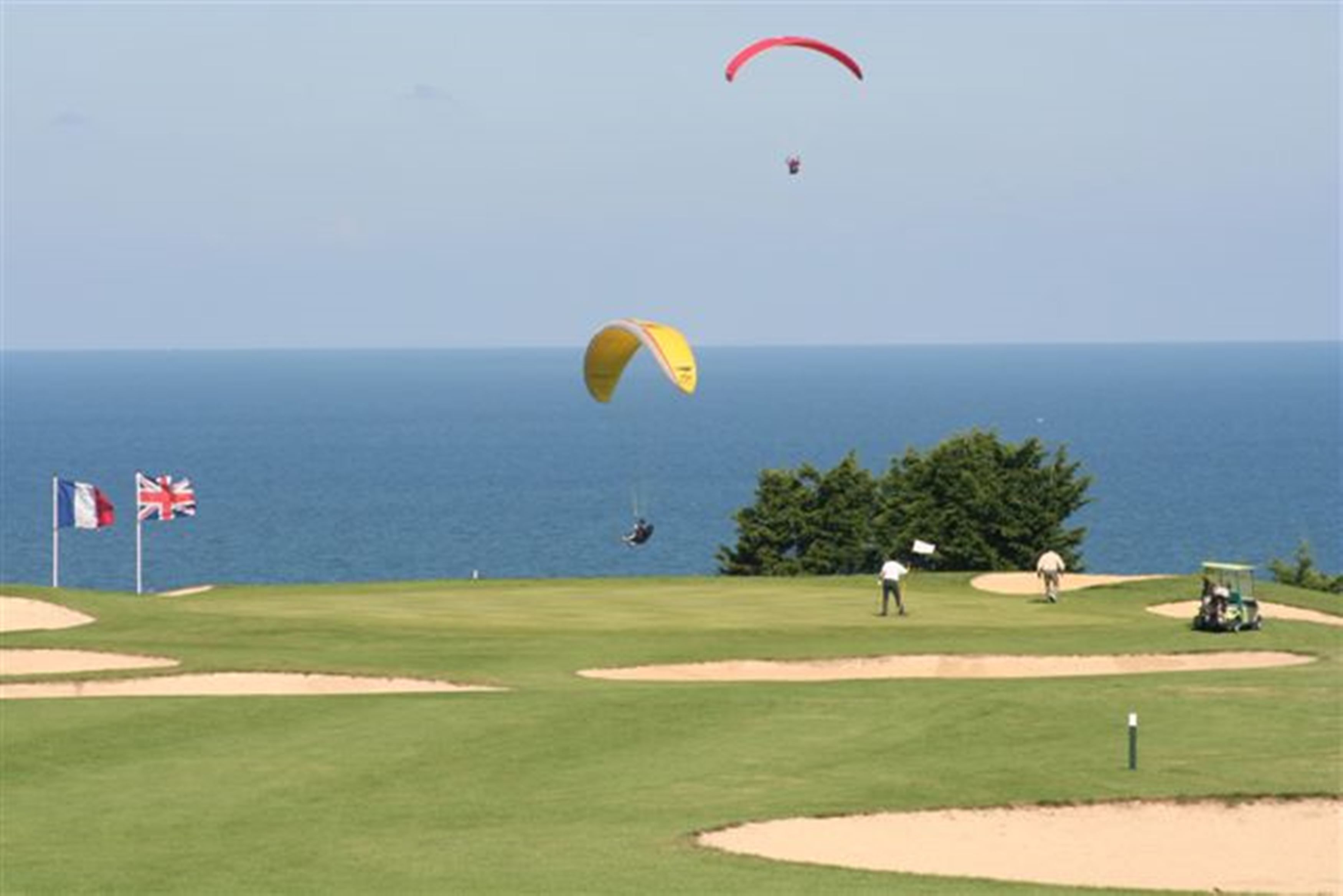 A golf course with flags, a flagstick, and a body of water in the background.