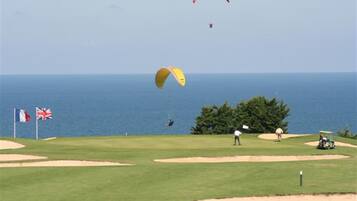 A golf course with flags, a flagstick, and a body of water in the background.