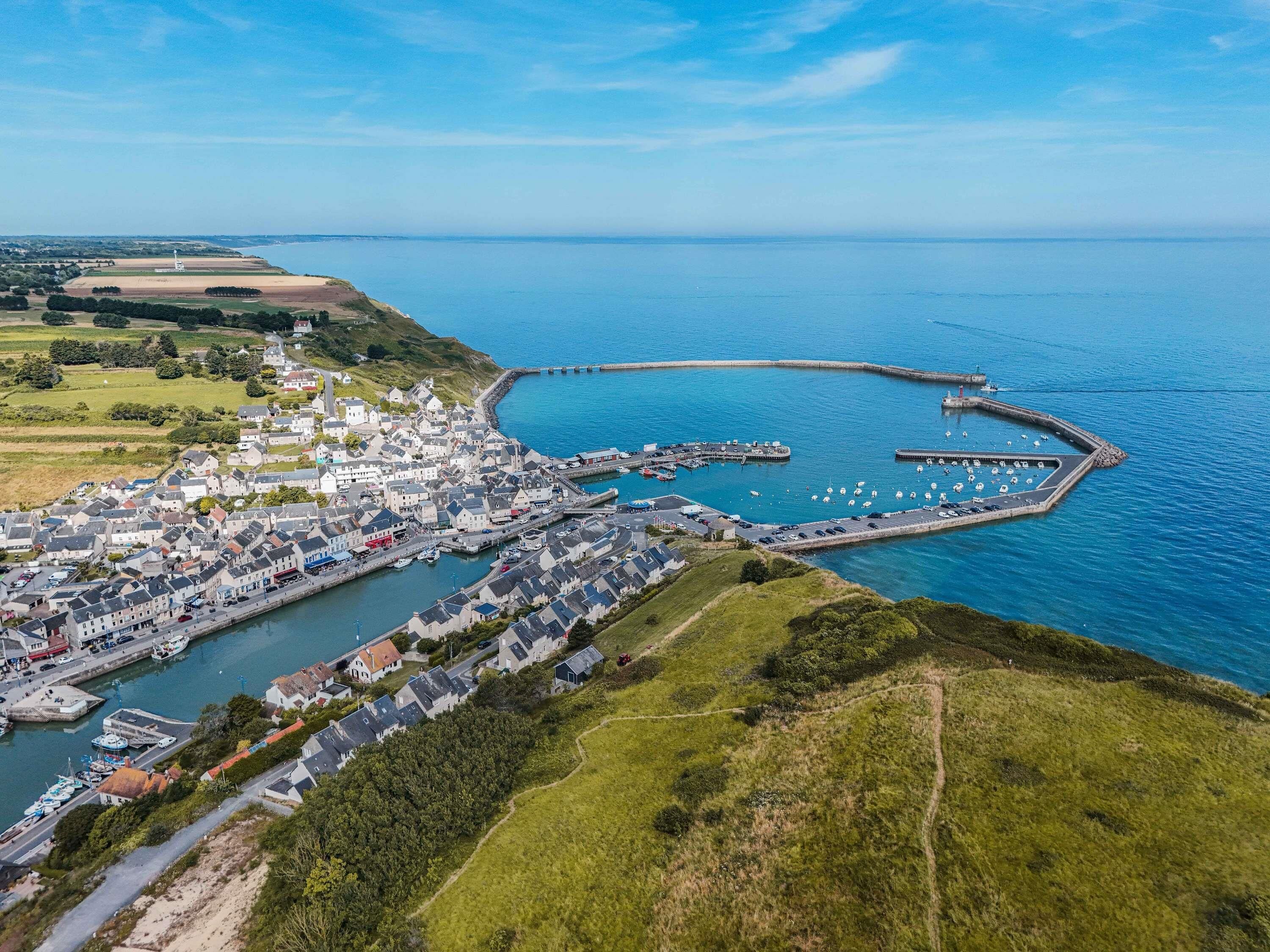 Vista aérea de un pueblo costero con un puerto deportivo, casas y un faro.