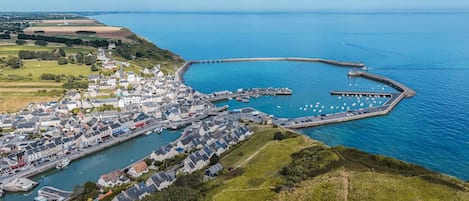 Vista aérea de un pueblo costero con un puerto deportivo, casas y un faro.