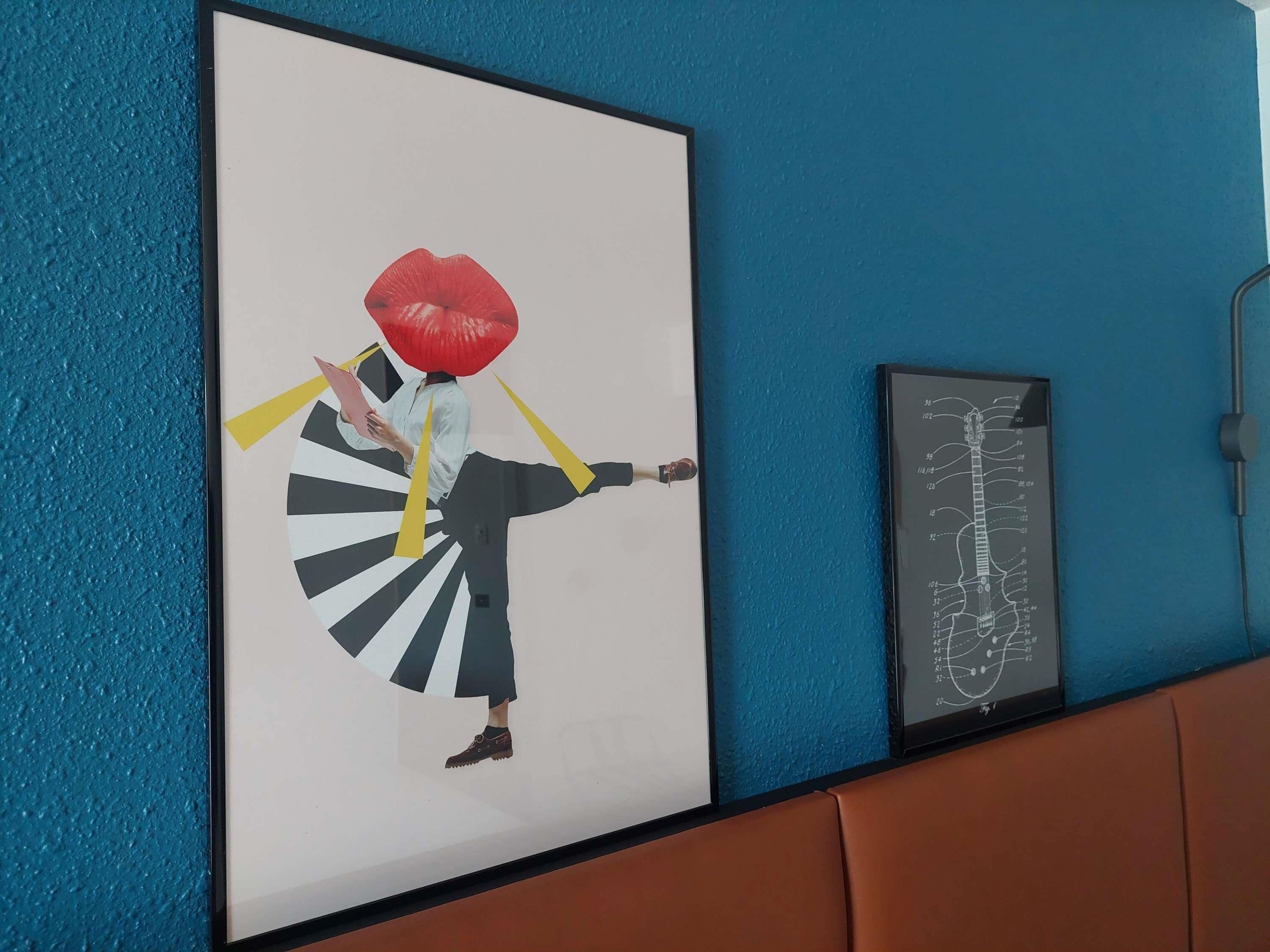 Ein gerahmtes Kunstwerk zeigt eine Person mit einem roten Gegenstand auf dem Kopf, einem Fächer und einer Gitarre an der Wand.