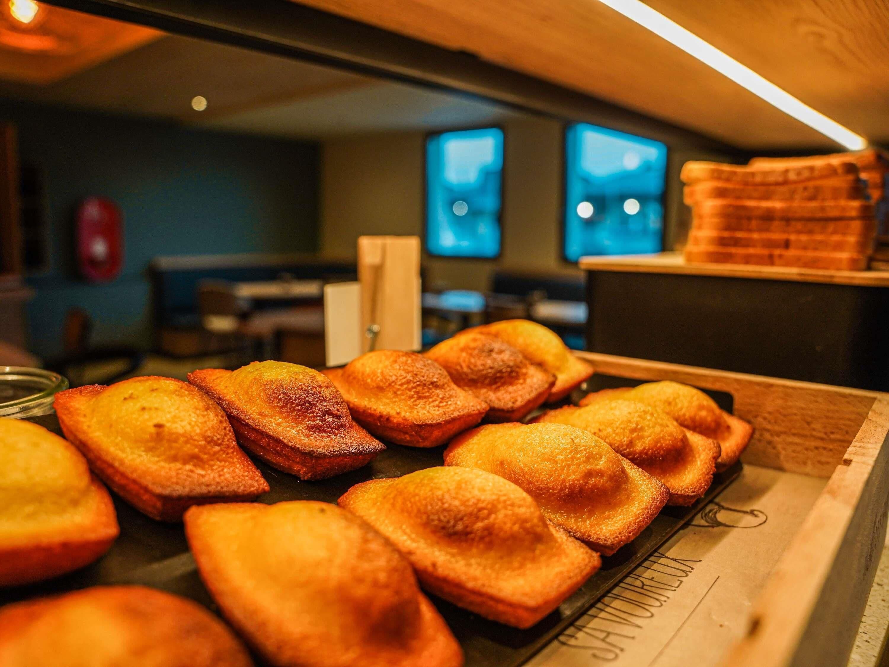 Una exhibición de pasteles dorados en una panadería, con un mostrador y dos monitores al fondo.