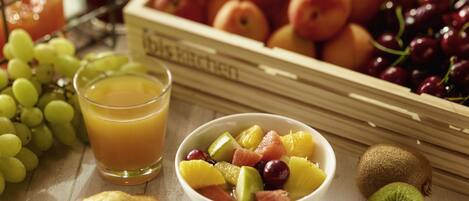 Une table mise pour le petit-déjeuner avec un bol de fruits, un verre de jus d’orange et une variété de fruits et de légumes frais.