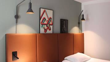A hotel room with a brown headboard, two beds, a wall-mounted artwork, and two wall-mounted lamps.