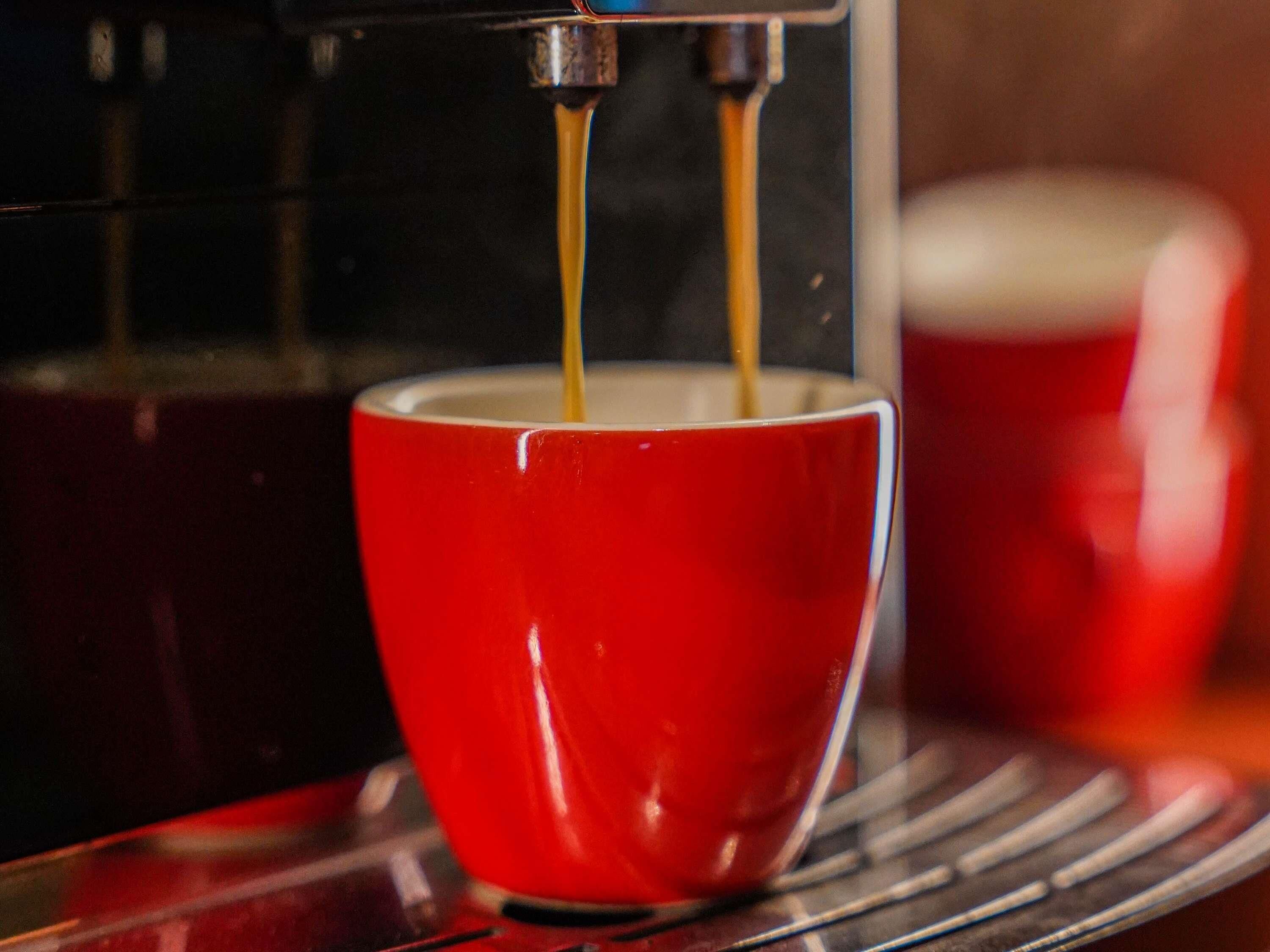 Una taza roja sobre una bandeja, con café sirviéndose dentro.