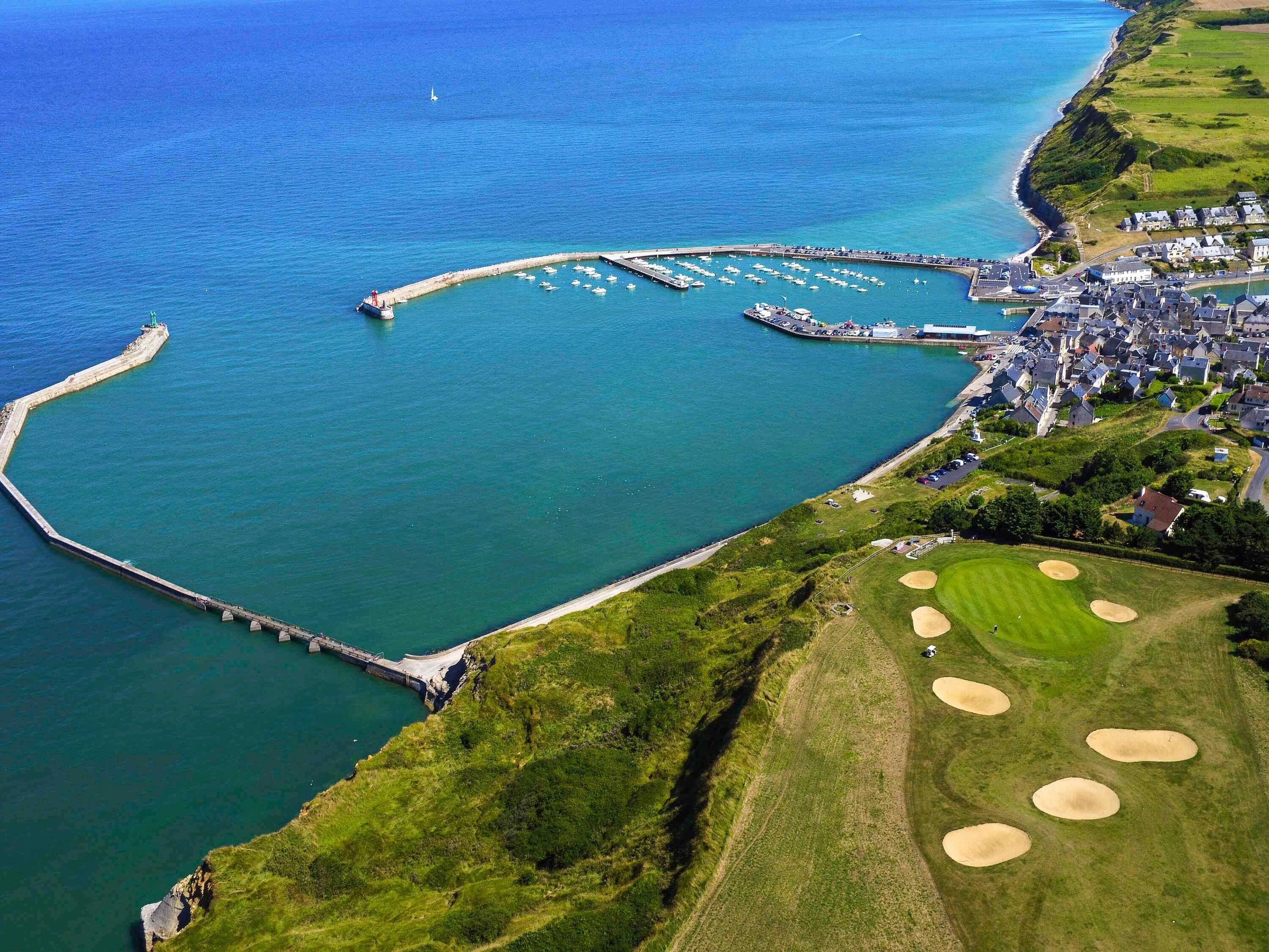Luftaufnahme einer Küstenstadt mit Hafenanlage, Golfplatz und Wohngebiet.