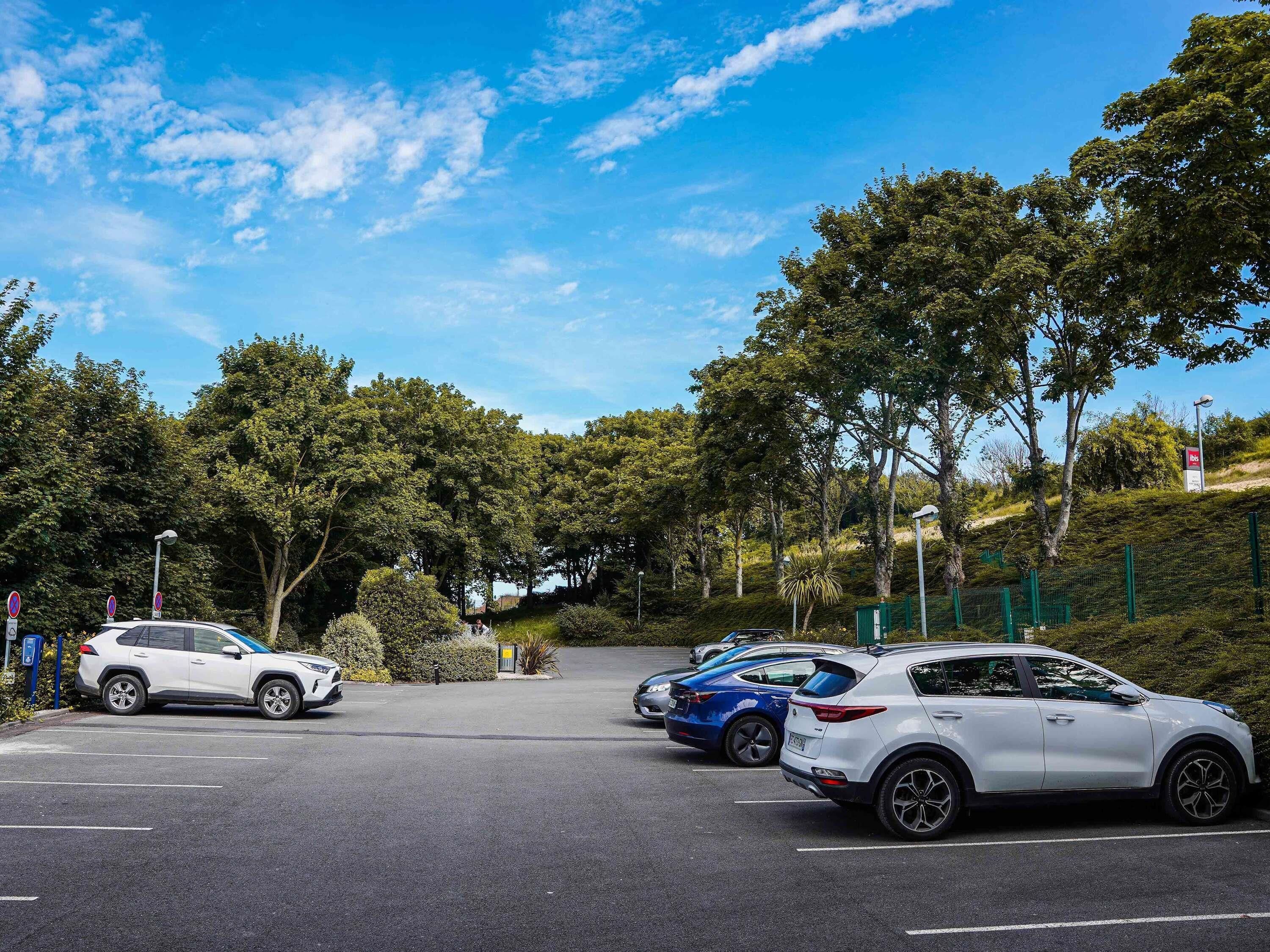 Un parking rempli de voitures, entouré d’arbres et avec un ciel dégagé.