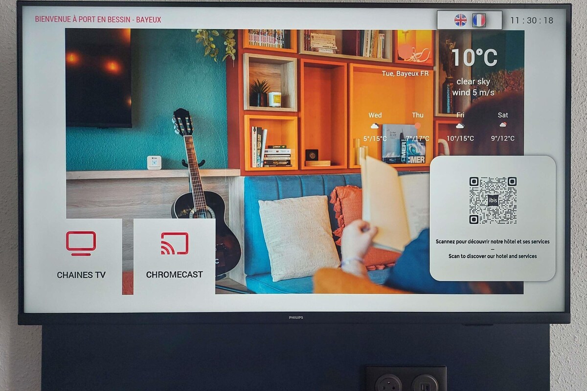 A television screen displaying a hotel welcome page with TV and Chromecast icons, a QR code, and a weather widget.