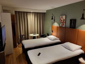 Una habitación de hotel con dos camas, un escritorio, una silla, un televisor y una cortina.