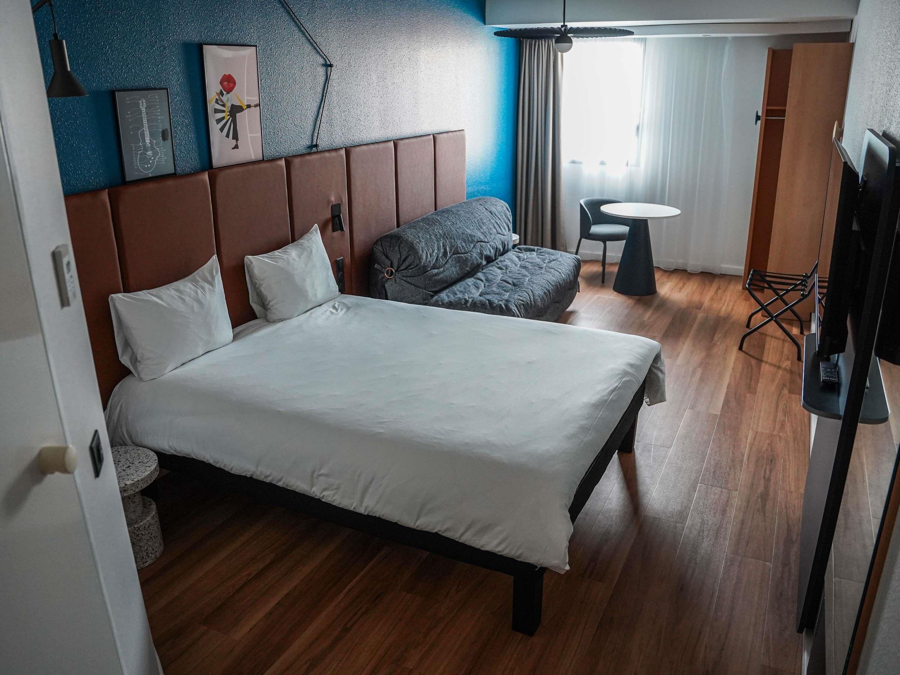 Habitación de hotel con cama, sofá, una mesita, televisor y ventana con cortinas.