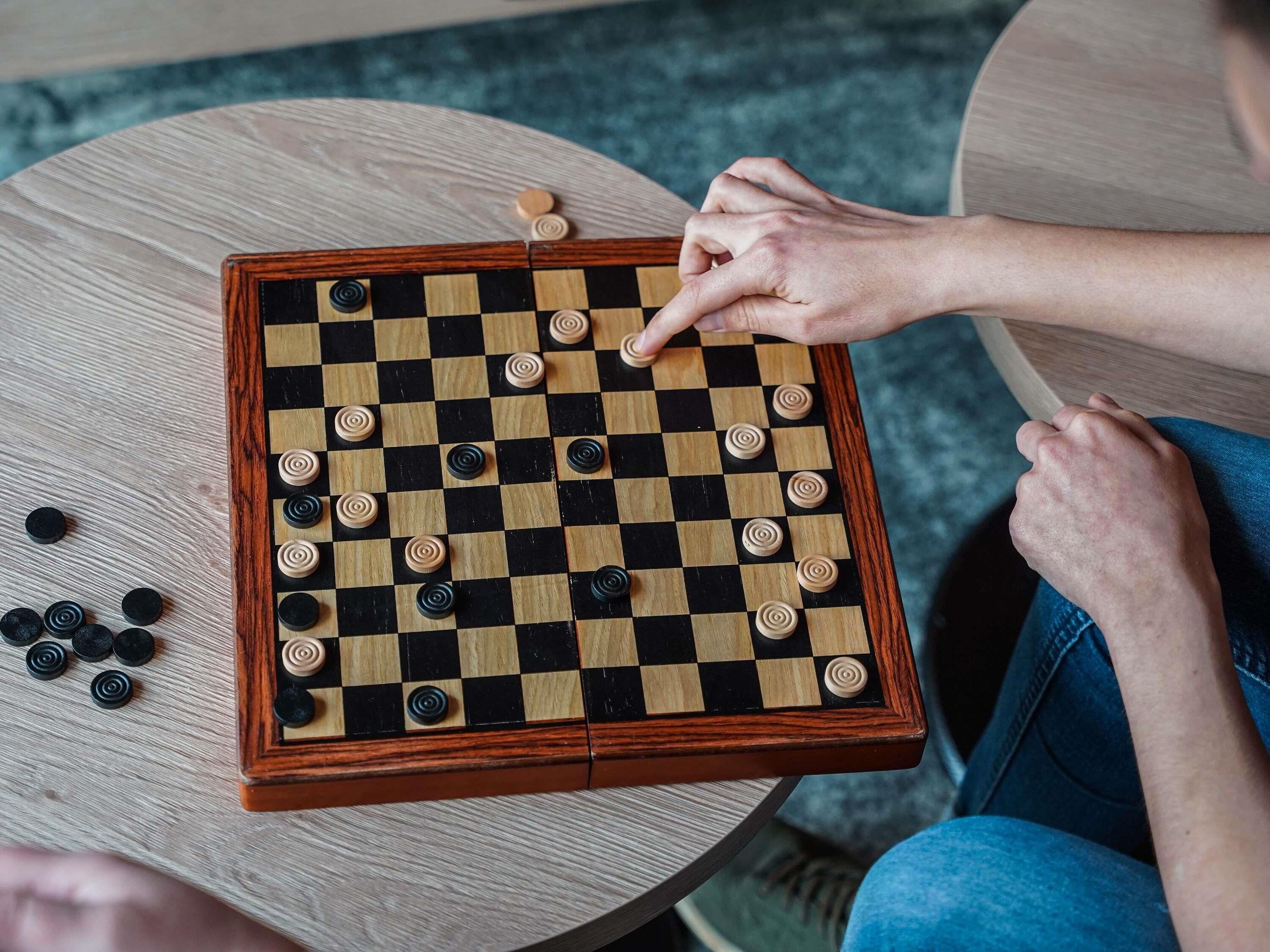 Un tablero de ajedrez sobre una mesa de madera redonda, con una persona jugando.