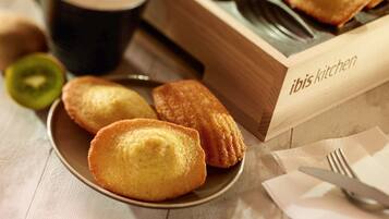 A wooden box labeled "ibis kitchen" with a plate of pastries and a cup of coffee on a table.