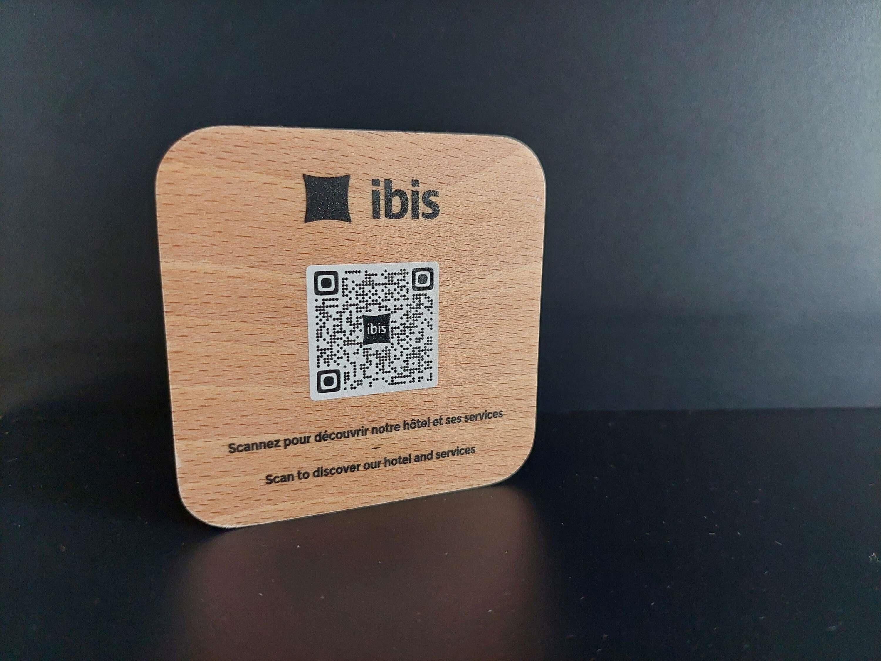 A wooden card with a QR code and the text "ibis" and "Scan to discover our hotel and services."
