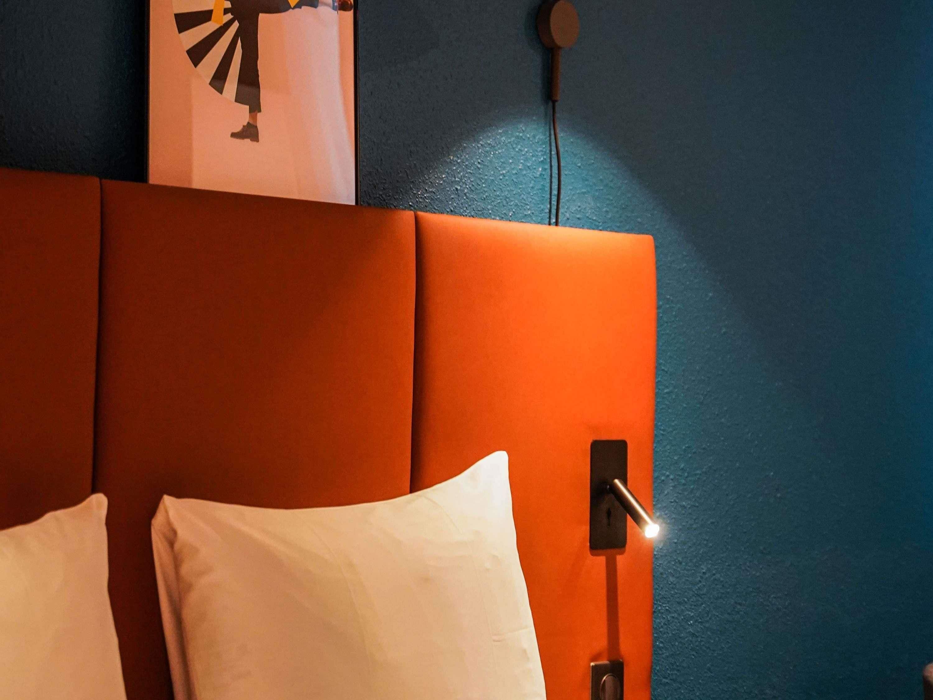 Un lit avec des oreillers blancs et une tête de lit adossée à un mur bleu.