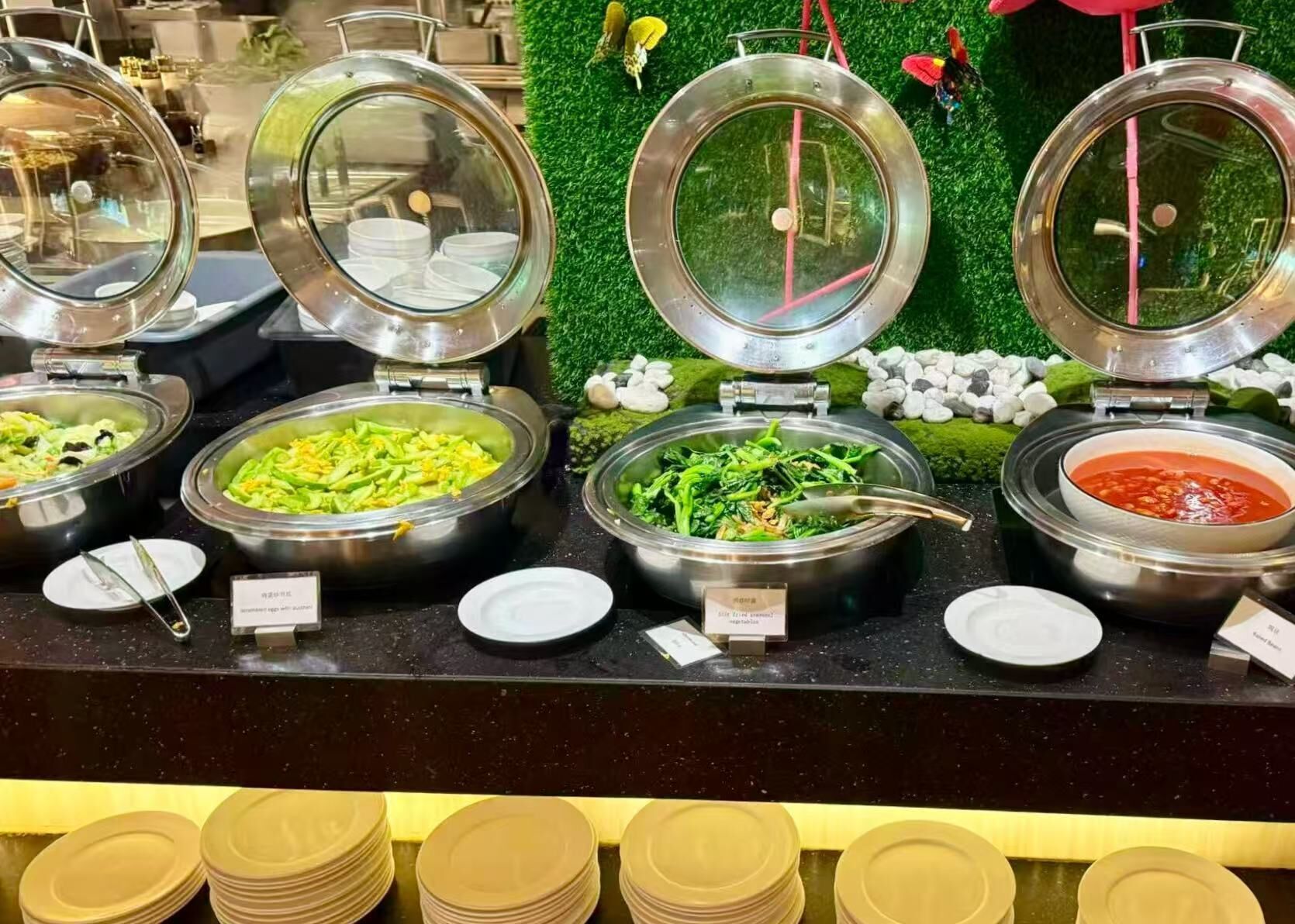 A buffet with various dishes, including a salad, a vegetable dish, and a red sauce.