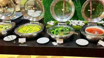 A buffet with various dishes, including a salad, a vegetable dish, and a red sauce.