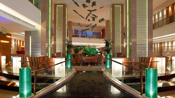 A modern hotel lobby with a central seating area, a glass staircase, and decorative elements on the ceiling. - Four Points by Sheraton Beijing, Haidian (Beijing)