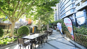 An outdoor cafe area with tables and chairs, surrounded by greenery and a building in the background. - Four Points by Sheraton Beijing, Haidian (Beijing)