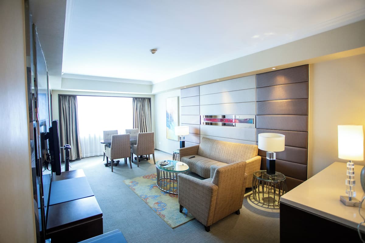 Quarto de hotel com sofá, poltrona, mesa de jantar, cadeiras e televisão.