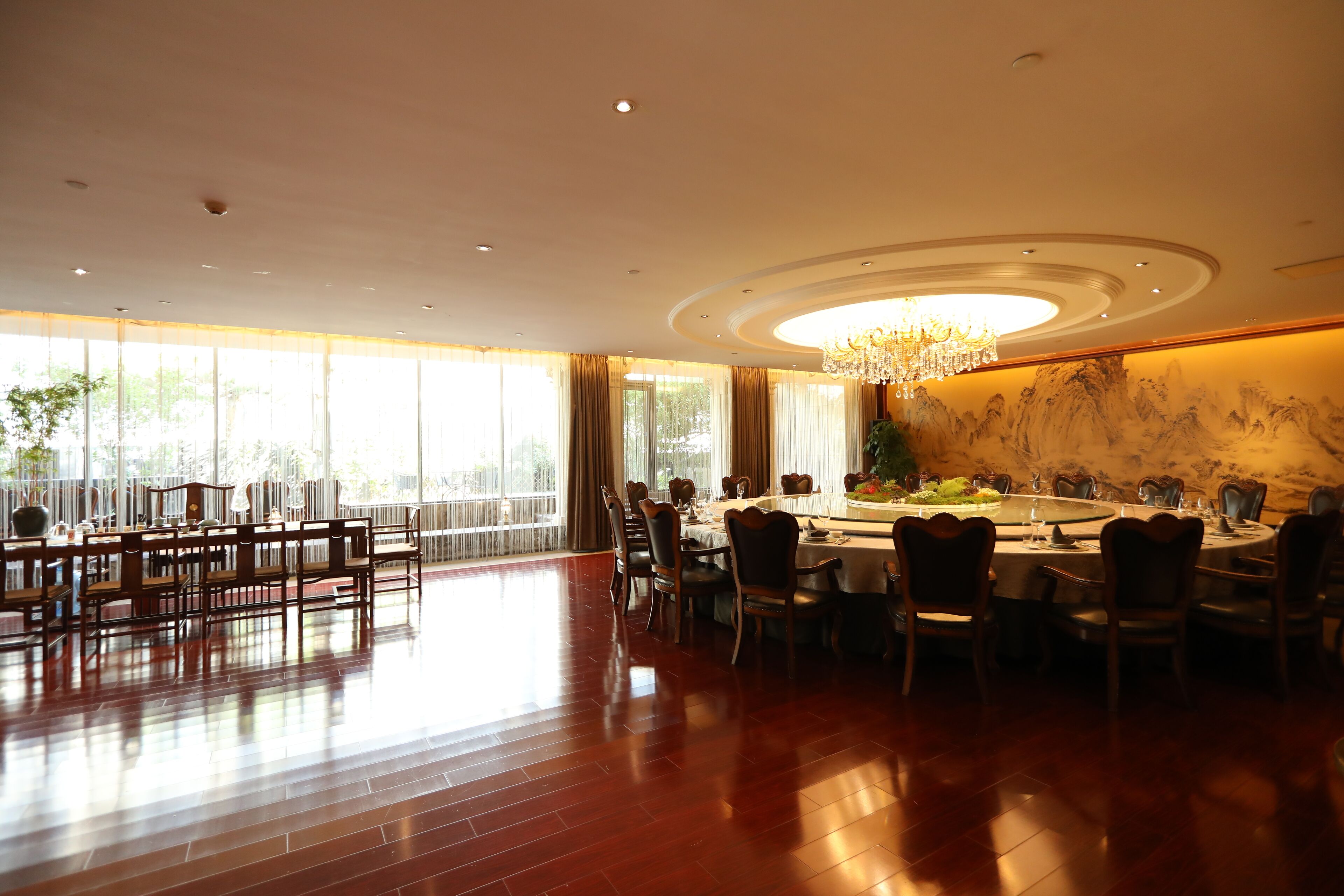 A spacious dining area with a high ceiling, chandeliers, and large windows.
