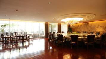 A spacious dining area with a high ceiling, chandeliers, and large windows.